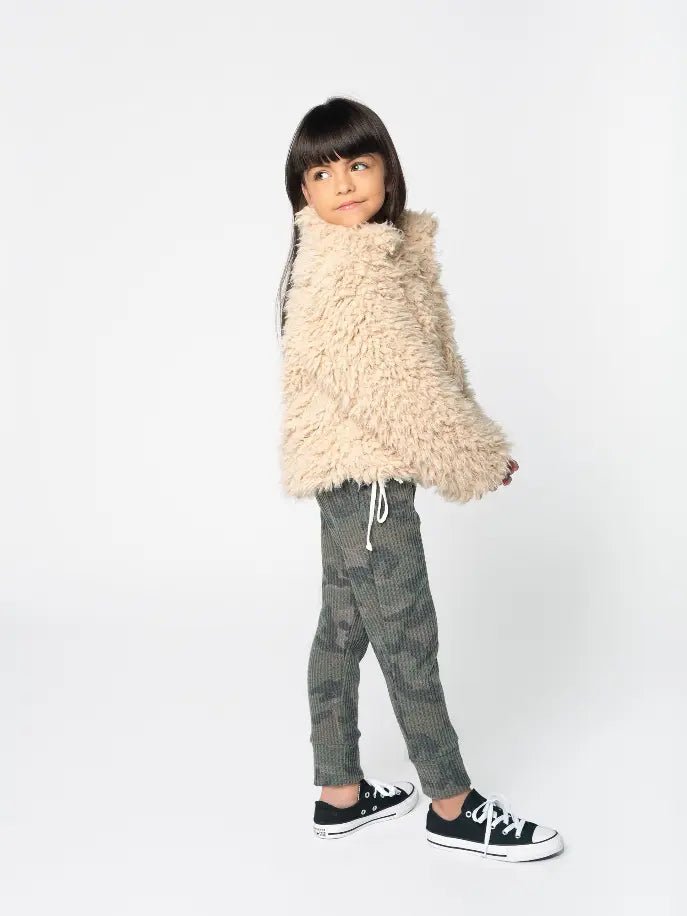 Tan faux fur jacket with a cozy fit, paired with olive green camo joggers and black sneakers. Perfect for kids.
