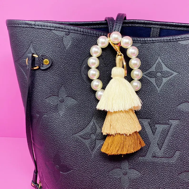 Black leather tote bag with a pearl and tassel charm in cream, caramel, and brown accents.