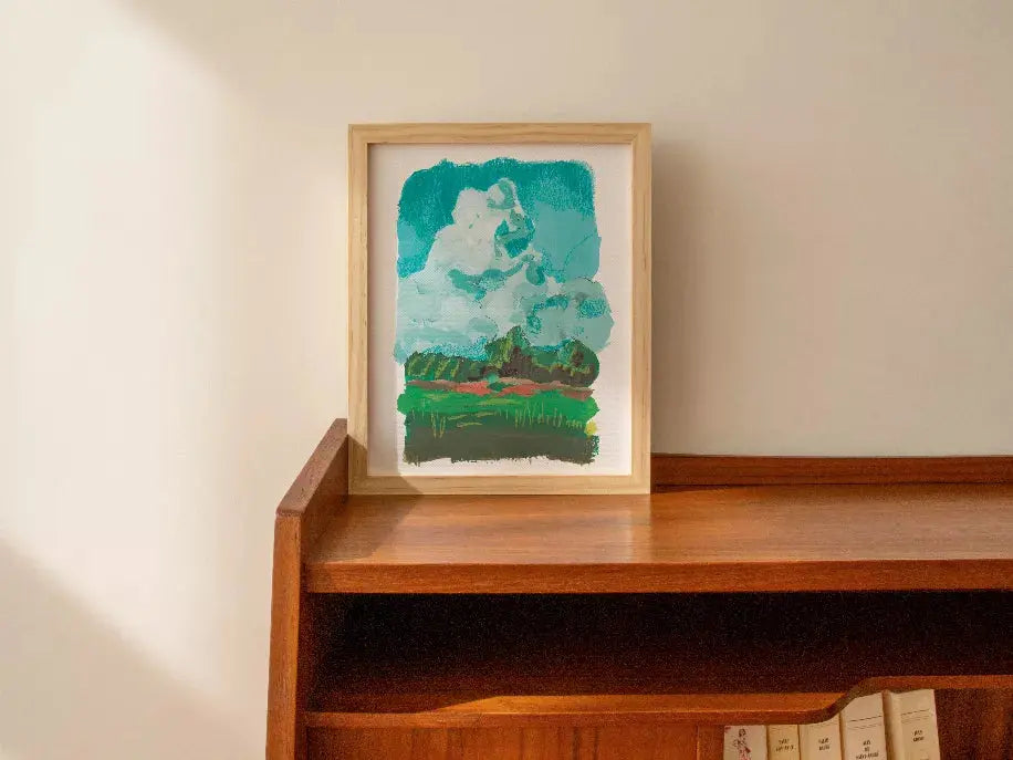 Framed abstract art print featuring turquoise clouds and green landscape on wood shelf, perfect for modern decor.