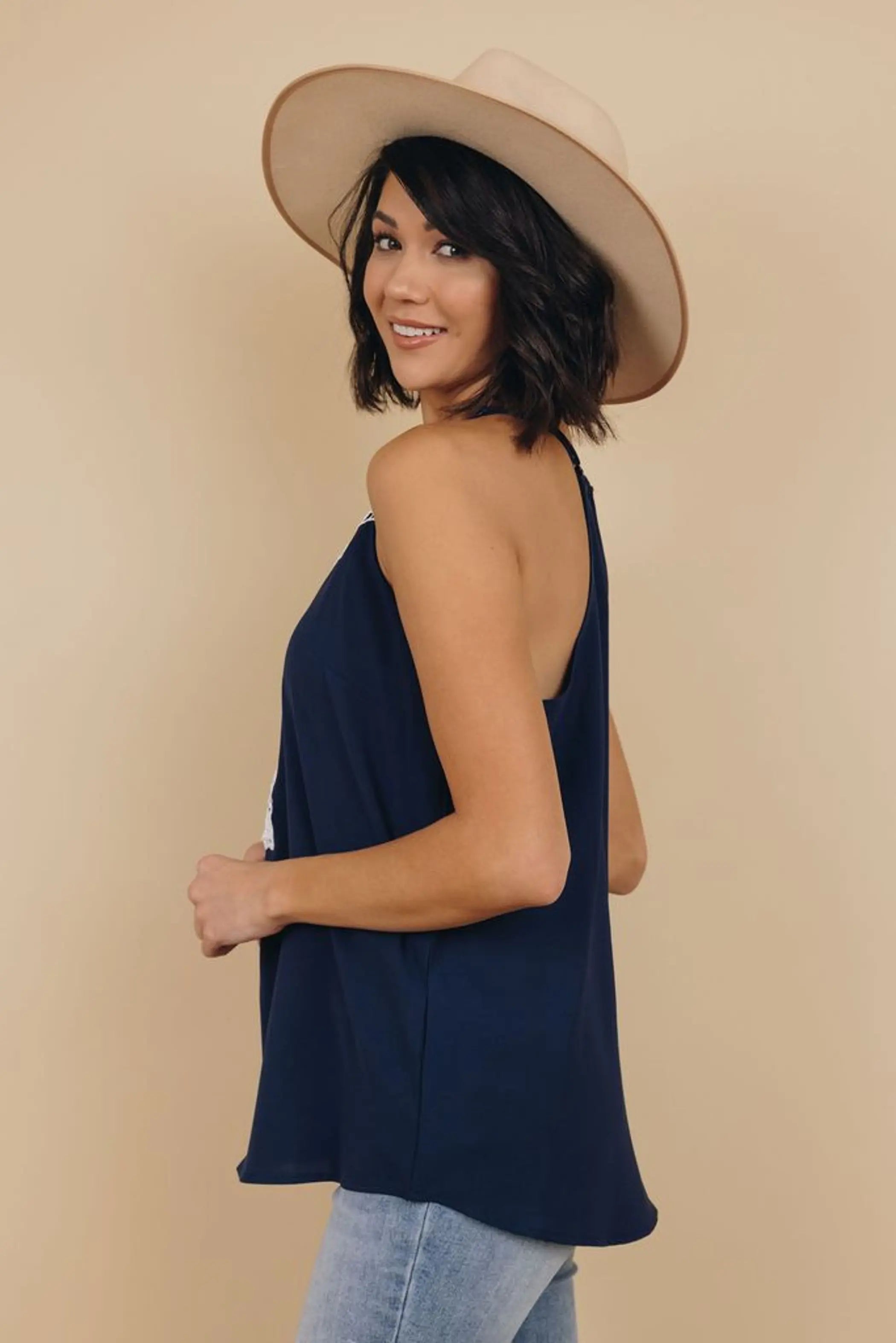 Model wearing a navy blue sleeveless top with a relaxed fit, paired with a cream wide-brim hat and light-wash jeans.