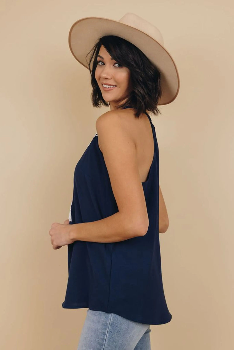Model wearing a navy blue sleeveless top with a relaxed fit, paired with a cream wide-brim hat and light-wash jeans.