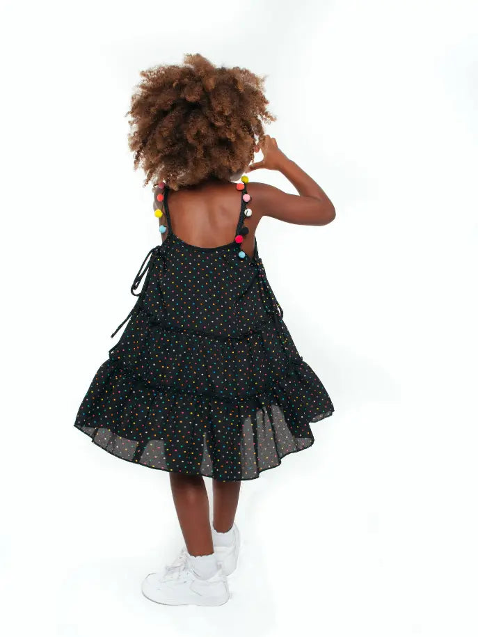 Black polka dot dress with ruffled tiers and colorful pom-poms, perfect for kids' casual summer wear.