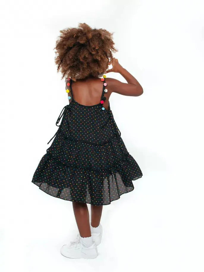 Black polka dot dress with colorful pom-poms, tiered design, perfect for kids' summer fashion.