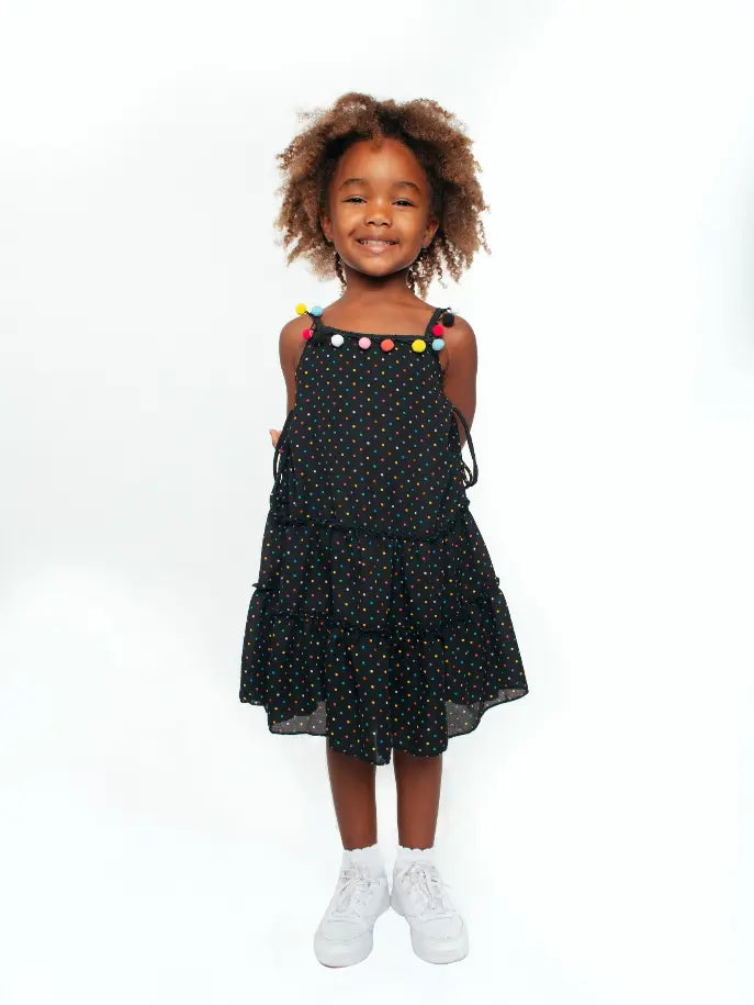 Black polka dot tiered dress with colorful pom-pom accents for girls, perfect for summer outings.
