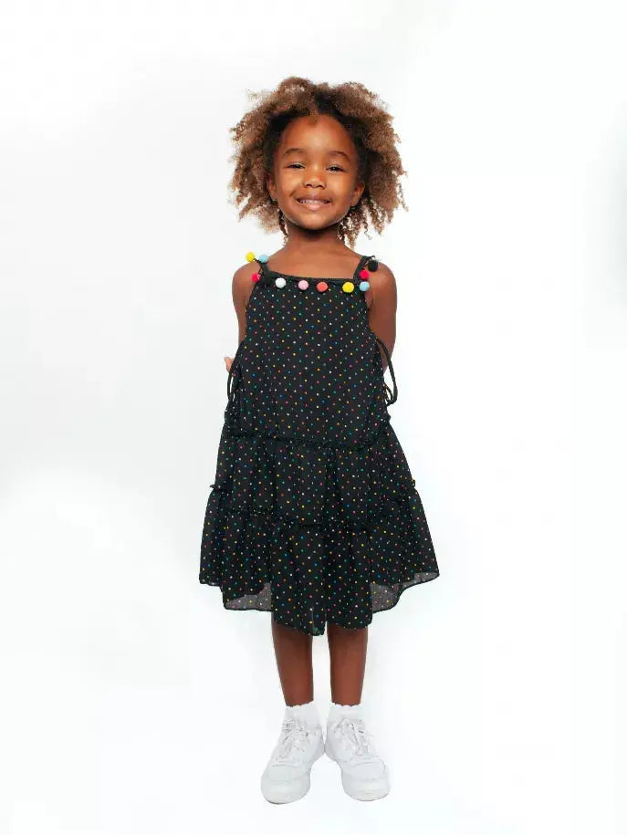 Black polka dot dress with colorful pom-poms, ruffled hem, and adjustable straps for girls, perfect for summer.
