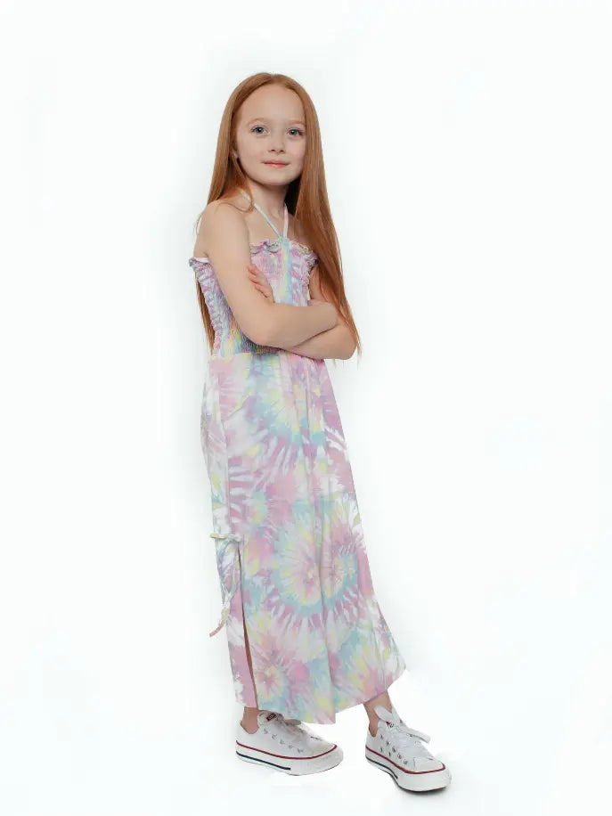Girl's pastel tie-dye maxi dress with smocked bodice, featuring adjustable straps and side slit, paired with white sneakers.