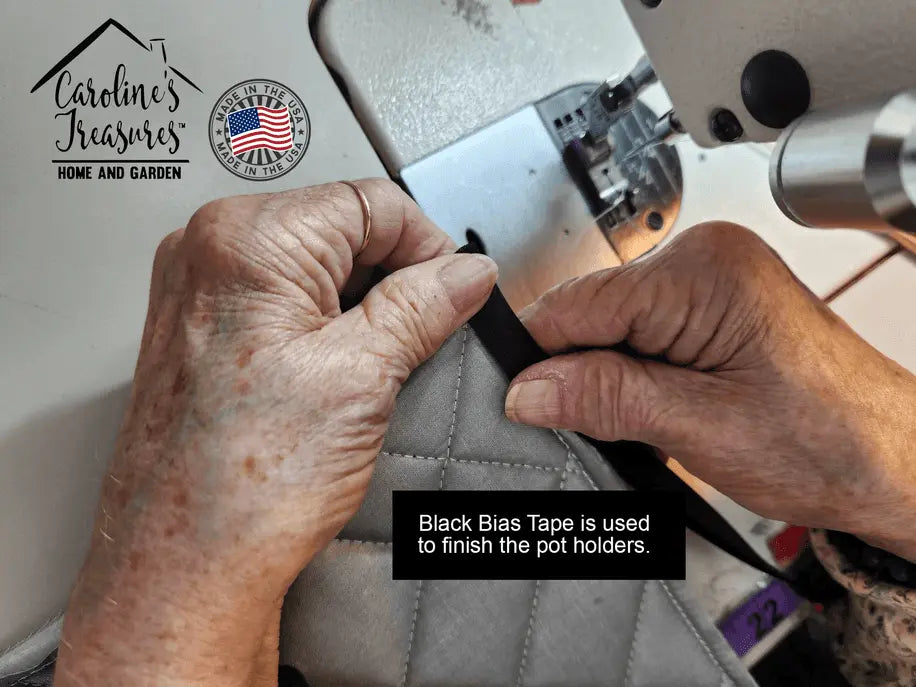 Hands sewing black bias tape to finish gray quilted pot holders, showcasing craftsmanship and quality materials.