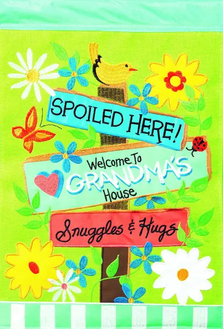 Colorful fabric garden sign with flowers, bird, and text: "Spoiled Here! Welcome to Grandma's House, Snuggles & Hugs."