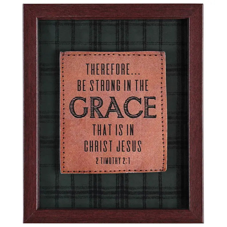 Framed inspirational wall art featuring brown leather patch with black text on a dark plaid background.