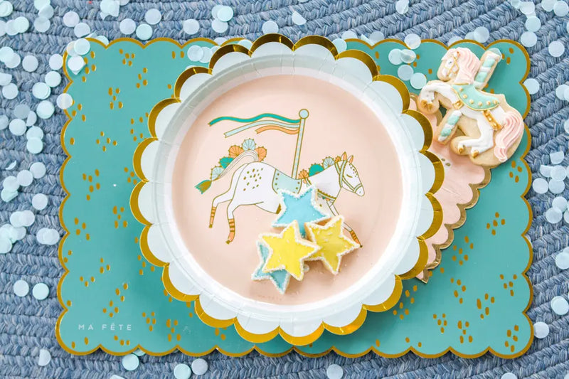 Scalloped pastel plate with carousel horse design, gold trim, and star-shaped cookies on a teal placemat.