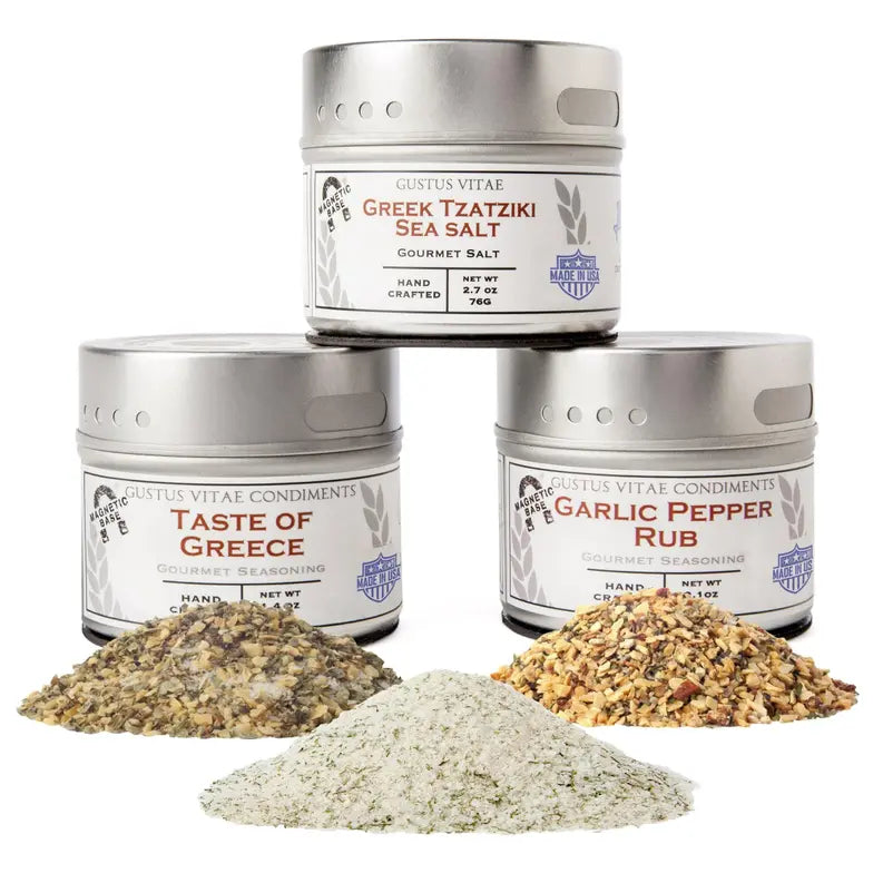 Three gourmet spice tins: Greek Tzatziki Sea Salt, Taste of Greece, and Garlic Pepper Rub with assorted spices.
