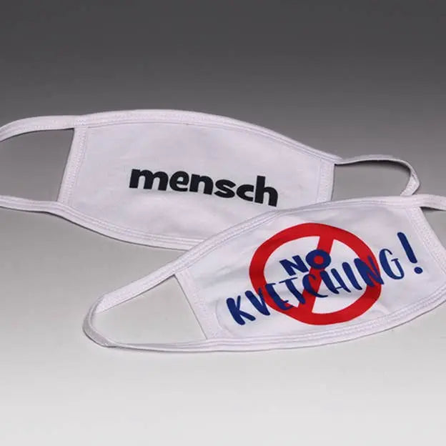 White cotton masks featuring "mensch" and "NO KVECHING!" designs in bold blue and red lettering.