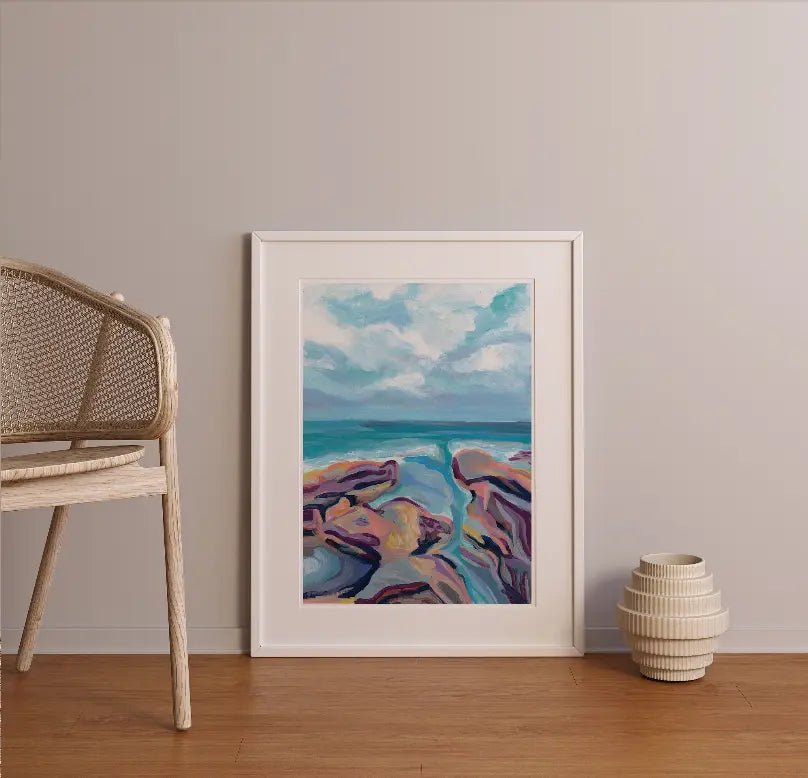 Framed abstract ocean artwork in vibrant blues and purples against a minimalist beige wall, complemented by natural decor.