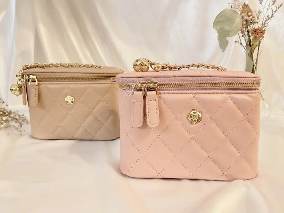 Quilted blush pink and beige cosmetic bags with gold chain accents and flower logo, perfect for stylish organization.