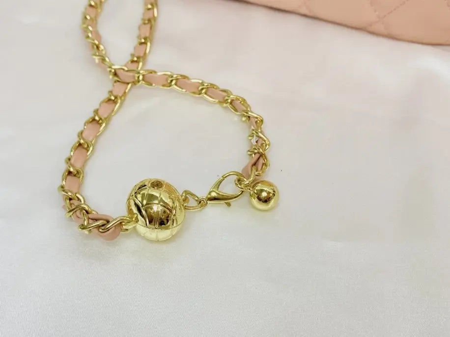 Gold chain strap with a textured ball and clip detail, paired with a soft pink material purse. Stylish and chic.