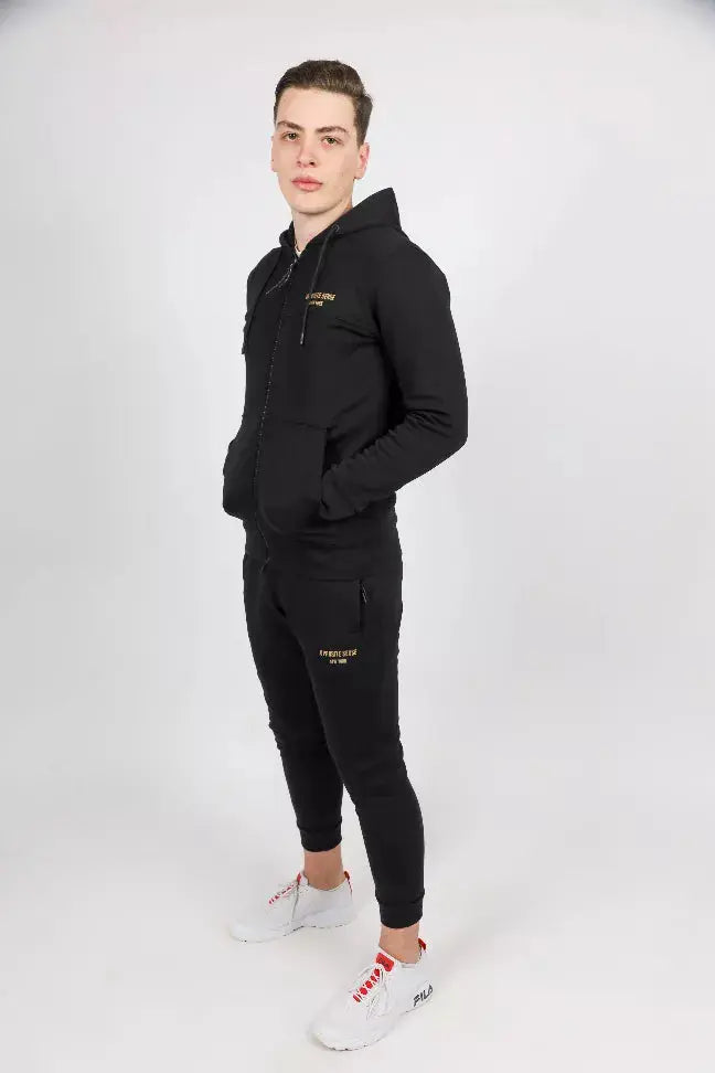 Black men's tracksuit in soft fabric with gold accents, featuring a zip-up hoodie and tapered pants, paired with white sneakers.