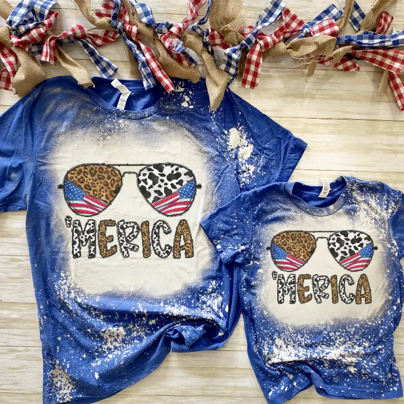 Men's and kids' blue graphic tees with leopard and cow print sunglasses, featuring an American flag and distressed finish.