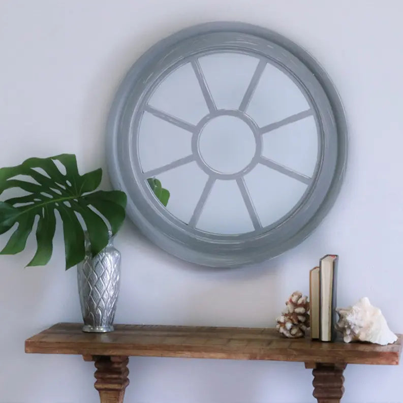 Gray circular wall mirror with a sunburst design, paired with a wooden shelf, greenery, and coastal decor elements.