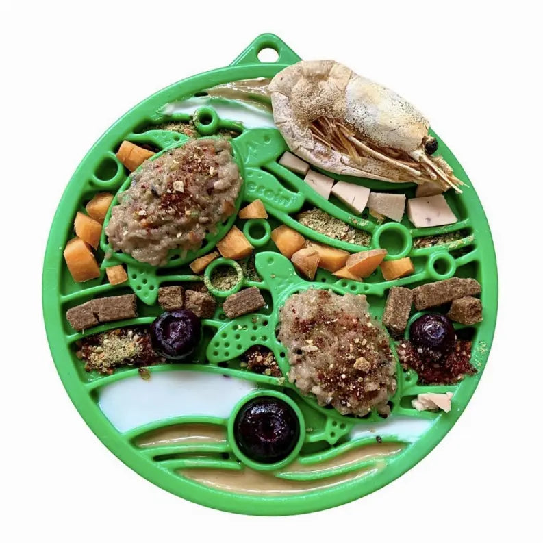 Green silicone pet feeding mat with turtle design, featuring assorted kibble, treats, and toppings for dogs or cats.