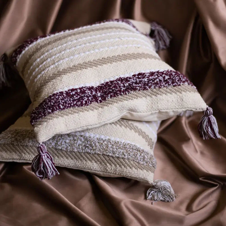 Soft beige and burgundy striped decorative pillows with tasseled corners, perfect for cozy home decor.