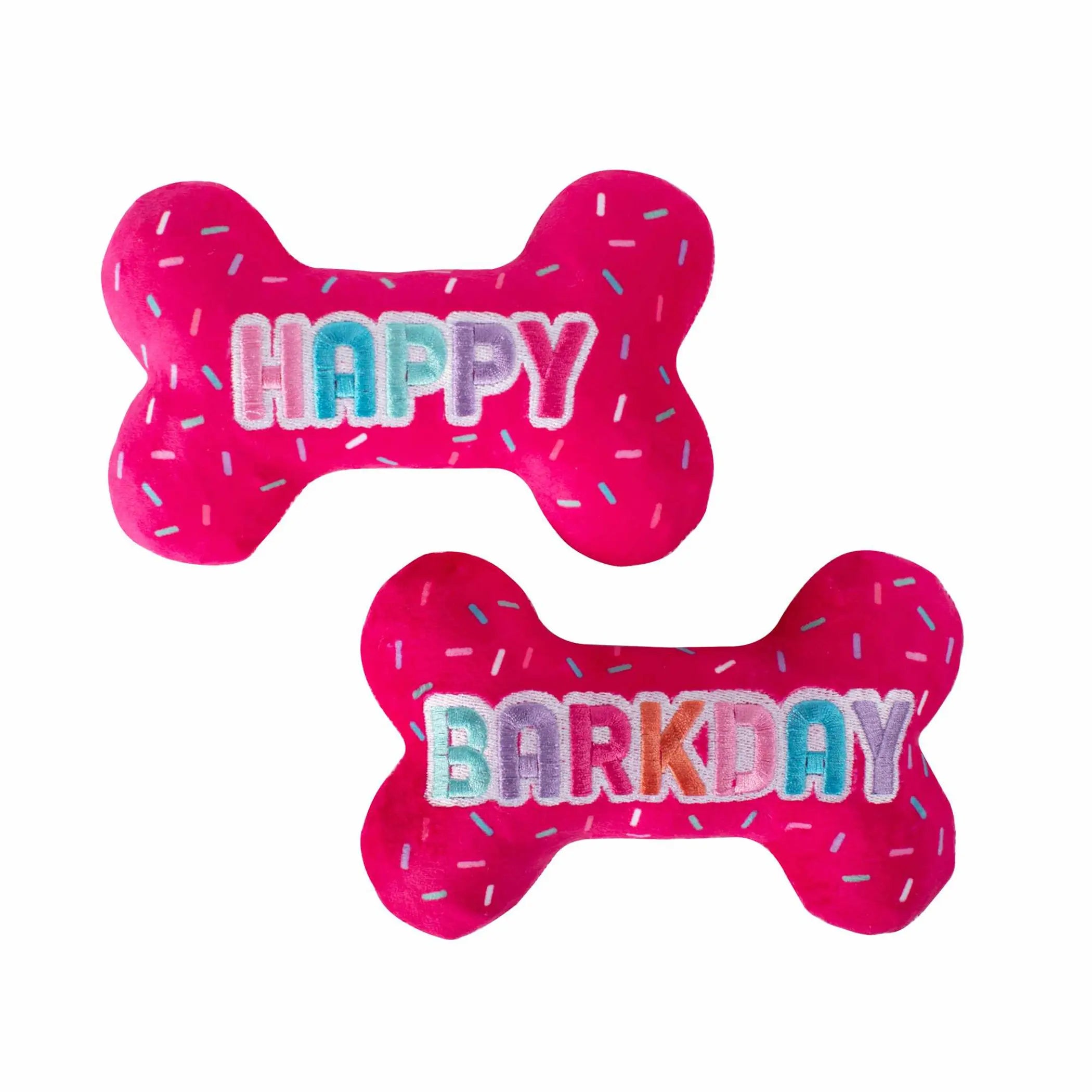 Bright pink plush dog toys in bone shape, featuring "HAPPY" and "BARKDAY" with colorful sprinkles. Perfect for celebrations!