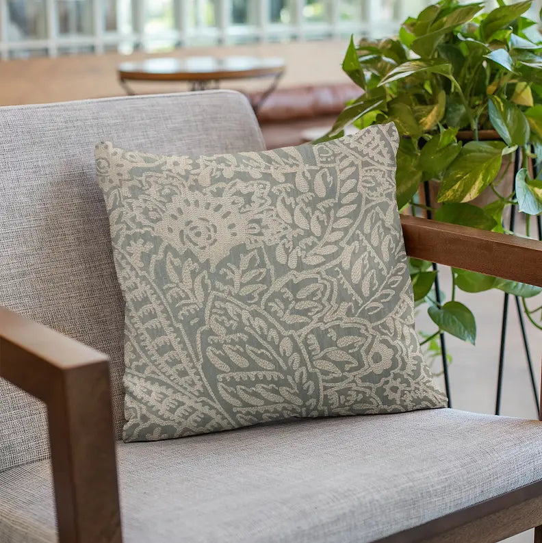 Elegant light blue floral patterned cushion in soft fabric, perfect for modern decor on a cozy armchair.
