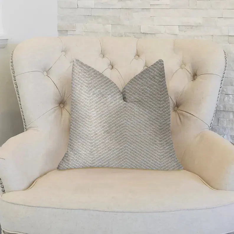 Light gray chevron pattern throw pillow on a tufted cream armchair, perfect for modern decor.