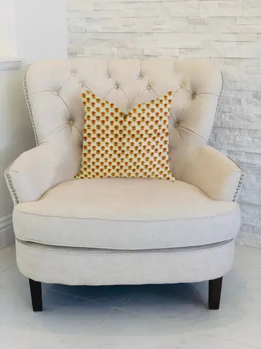 Cream tufted armchair with a vibrant orange star-patterned throw pillow, set against a white stone wall.