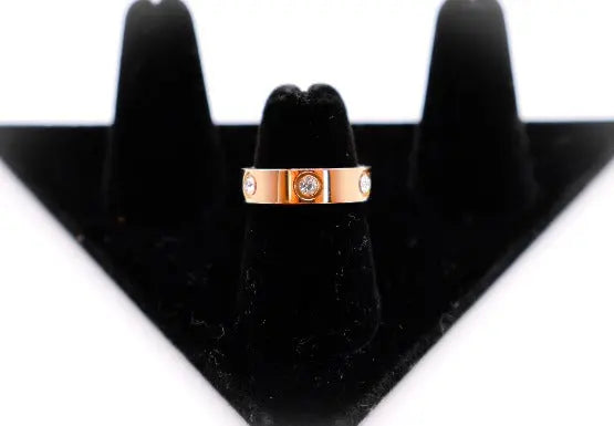 Rose gold band ring with three sparkling diamonds, displayed on a black velvet stand. Elegant and modern design.