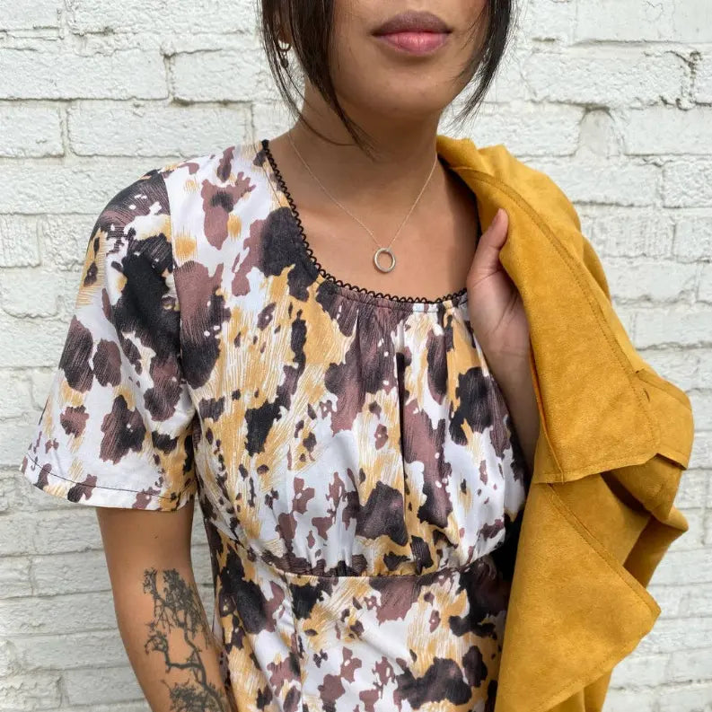 Trendy women's short-sleeve dress in brown and white leopard print with a black trim, paired with a mustard yellow jacket.