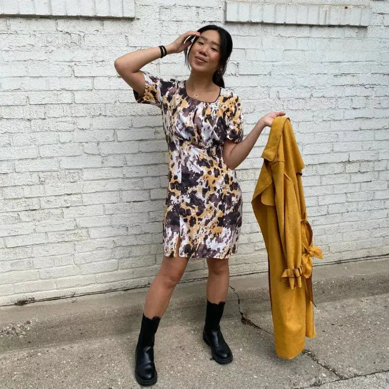 Multi-colored abstract print dress with short sleeves, paired with a mustard yellow coat and black ankle boots.