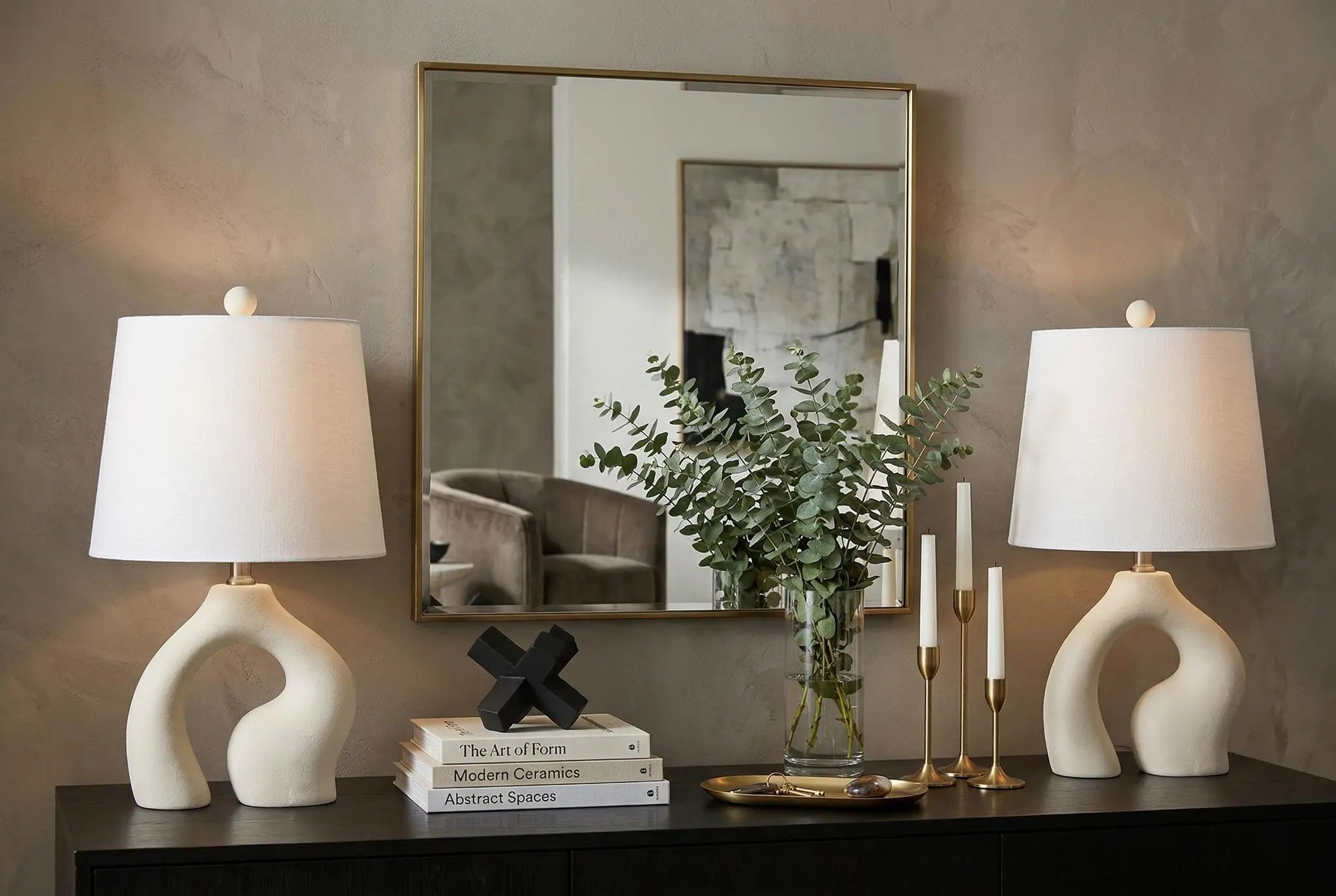 Modern beige ceramic table lamps with white shades, paired with a stylish mirror and elegant decor, in a chic living room setting.