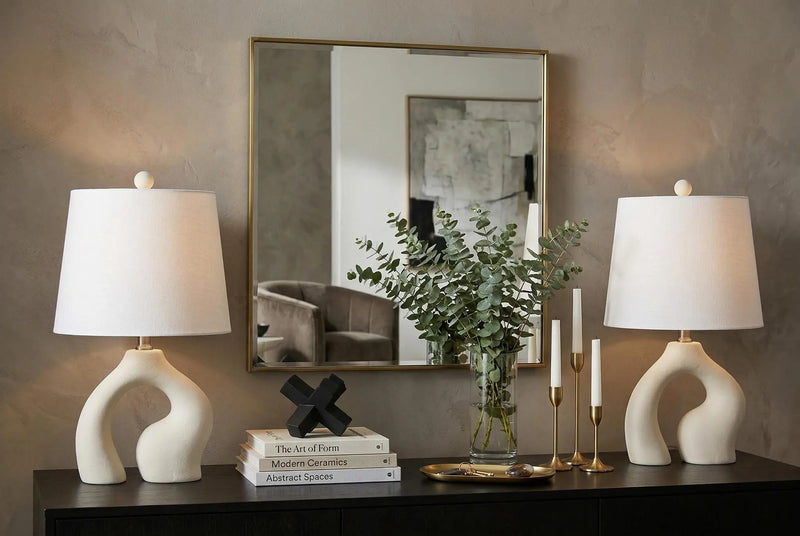Modern beige ceramic table lamps with white shades, paired with a stylish mirror and elegant decor, in a chic living room setting.