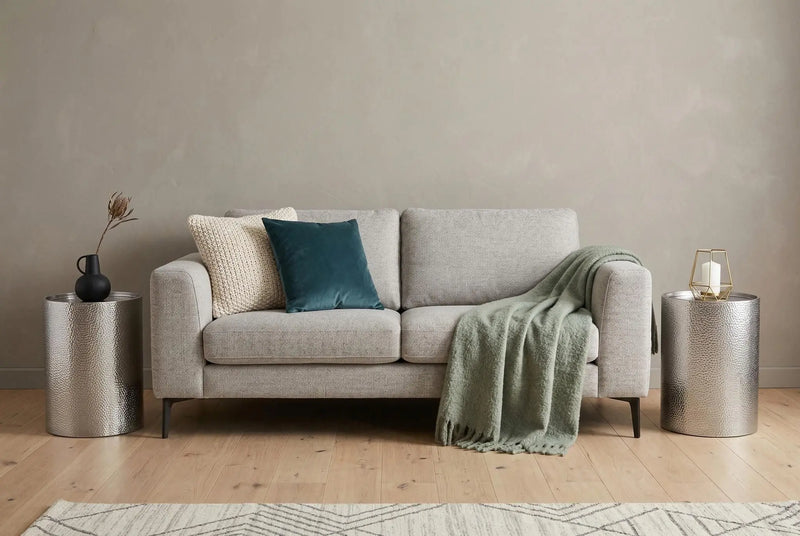 Light gray fabric sofa with teal and cream pillows, olive green throw, and silver side tables in modern living room.