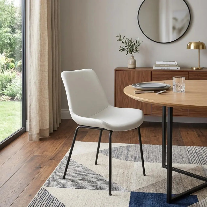 Modern white faux leather dining chair with black metal legs, set against a stylish wooden table and minimalist decor.