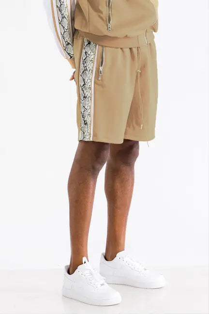 Beige athletic shorts with snake print side stripes, paired with white sneakers for a stylish casual look.