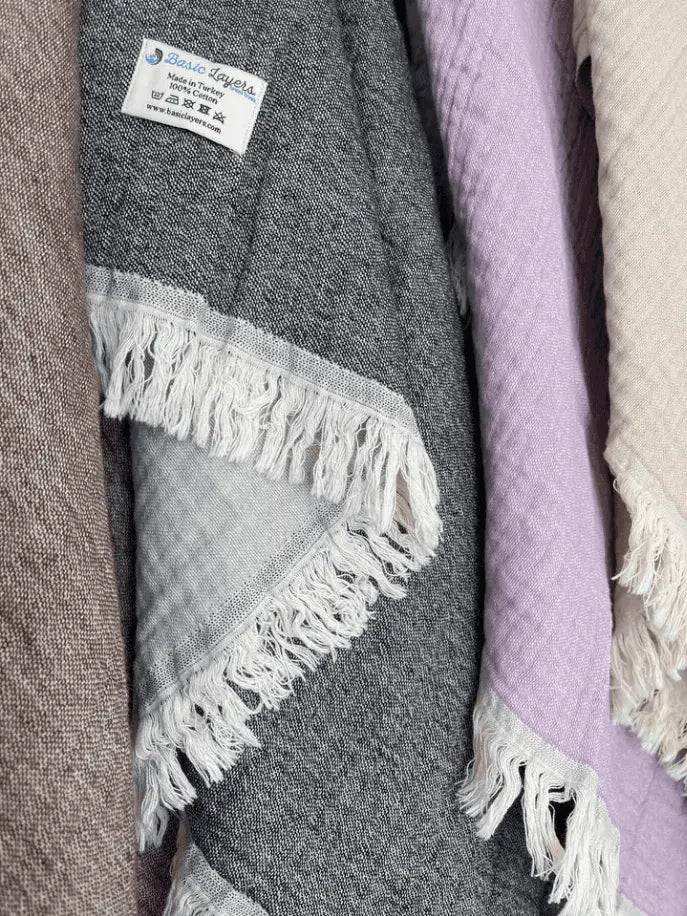 Cozy woven blankets in grey, lavender, and taupe with fringe edges, perfect for stylish home decor or gifting.