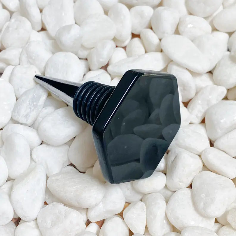 Black hexagon bottle stopper with a textured screw base, perfect for preserving wine or oil on a stylish tabletop.