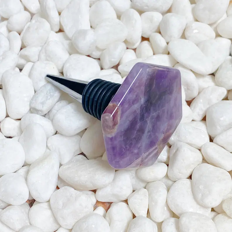 Amethyst wine bottle stopper with a hexagonal design and a black rubber base on white stones.