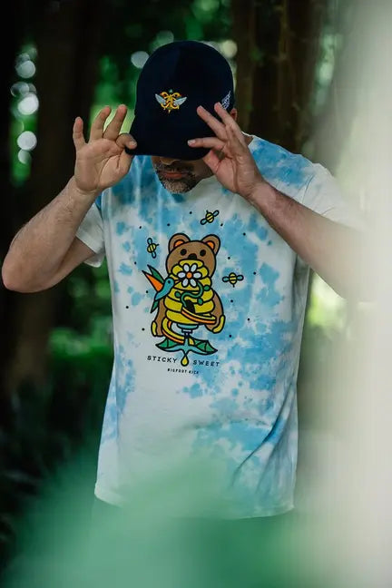 Men's tie-dye t-shirt featuring colorful bear graphic, made from soft cotton, paired with a navy cap.