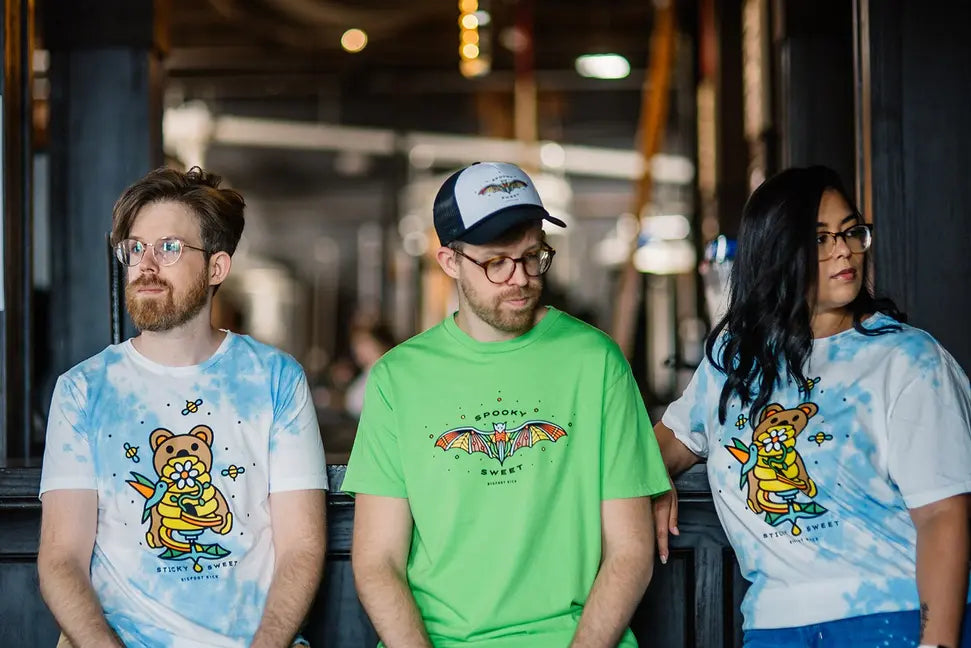 Three models in colorful T-shirts: blue tie-dye, lime green, and white with a cute graphic; casual style for Halloween.