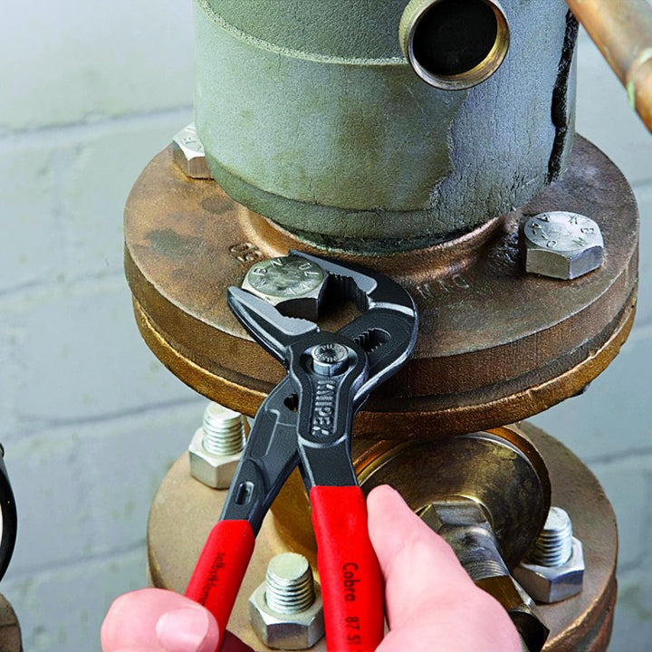 Narrow water pump pliers gripping a pipe fitting; red and black handles, Knipex
