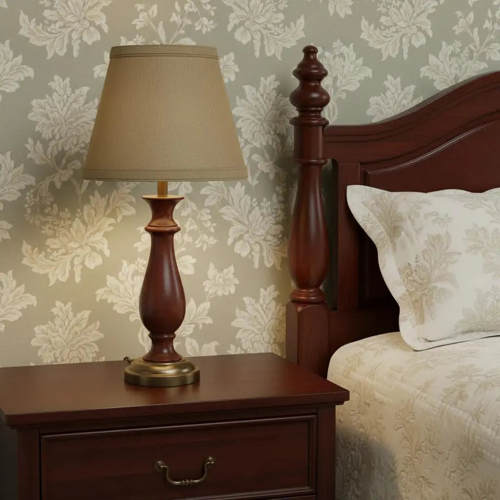 Brown wooden table lamp with a beige fabric shade, styled with elegant curves, next to a nightstand and floral wallpaper.