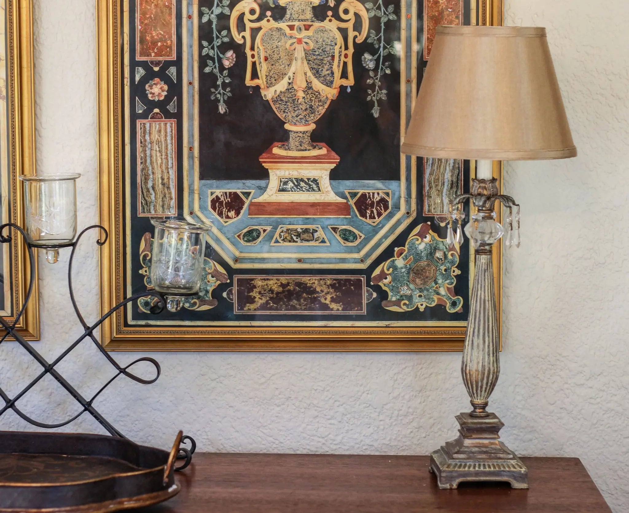 Vintage brass table lamp with a beige shade, set against ornate wall art, styled for elegant home decor.