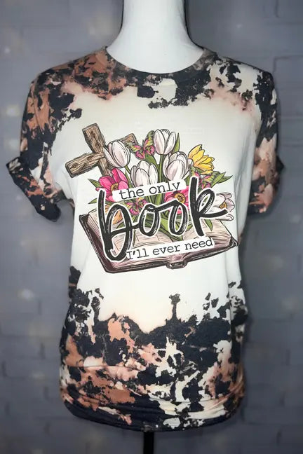 Vintage-style bleached t-shirt featuring floral design and "the only book I'll ever need" text in soft pink and green.
