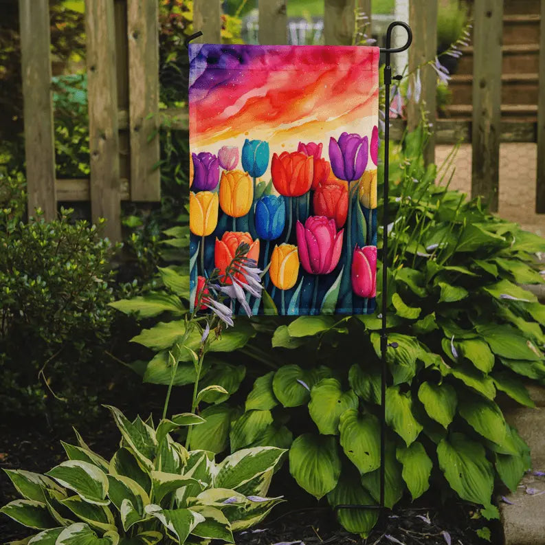 Vibrant tulip garden flag with multicolored flowers, hanging on a black metal stand, set against a lush green backdrop.