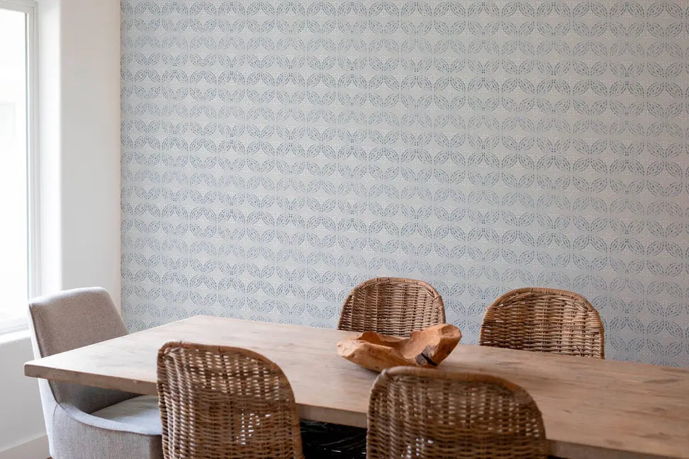 Light blue patterned wallpaper complements a rustic wooden dining table with woven chairs in a bright, modern setting.