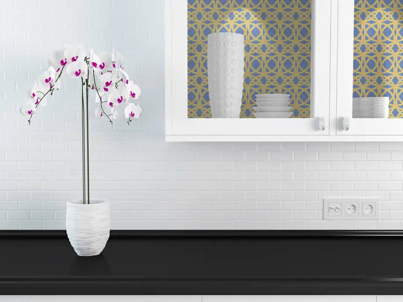 White orchid in a textured white vase, displayed against a gold and blue patterned backdrop in a modern kitchen.
