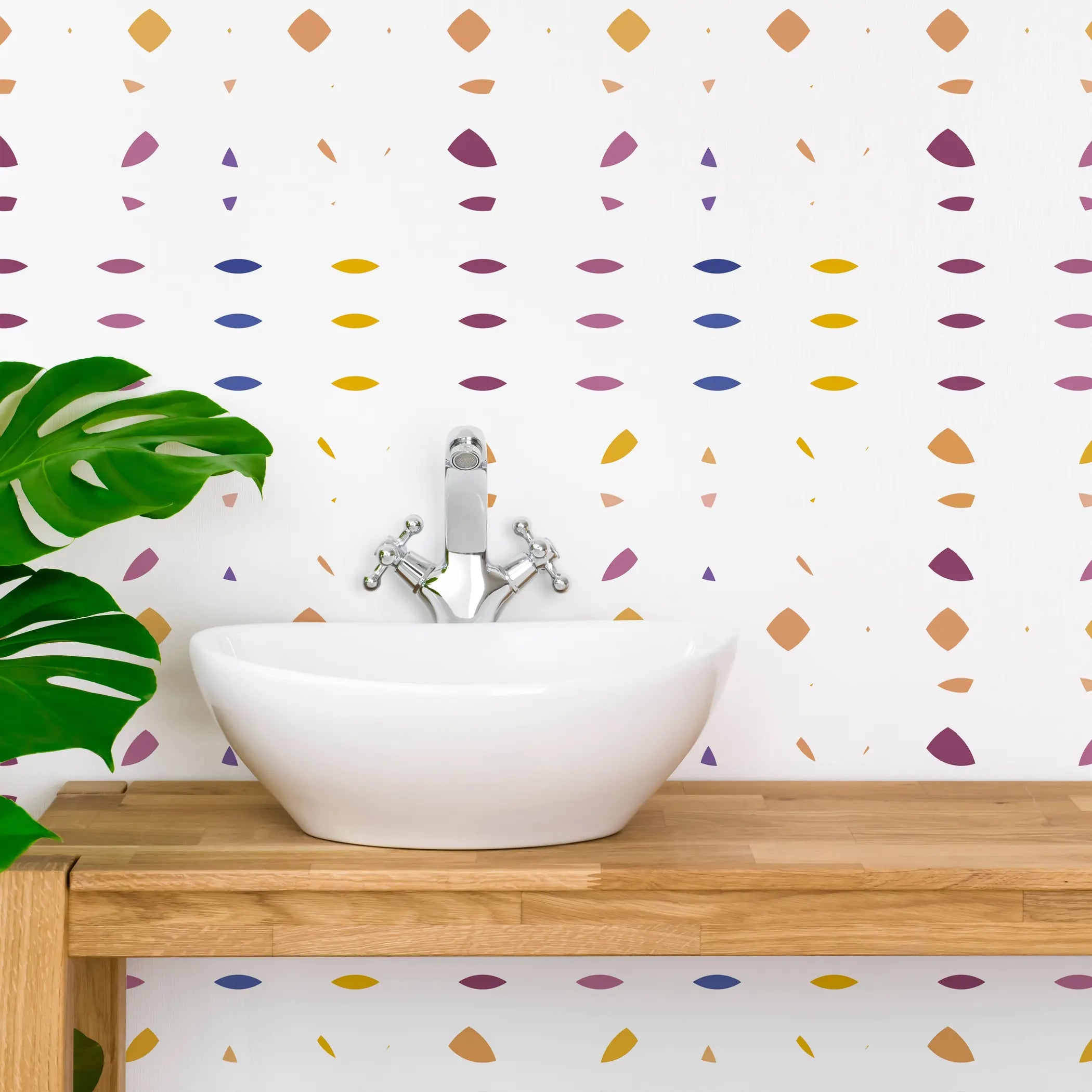 White ceramic basin on a wooden countertop against colorful abstract patterned wallpaper and green plant.