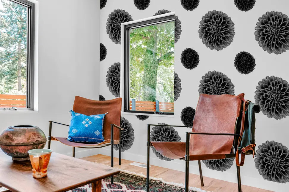 Brown leather chairs with black metal frames in a modern living room with floral black and white wallpaper.